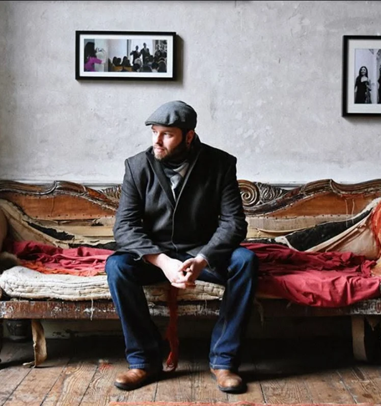 A man in a flat cap sitting on a worn antique bench