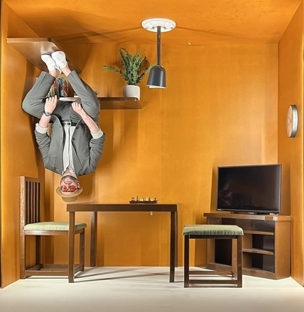 A man standing upside down on the ceiling of an orange room